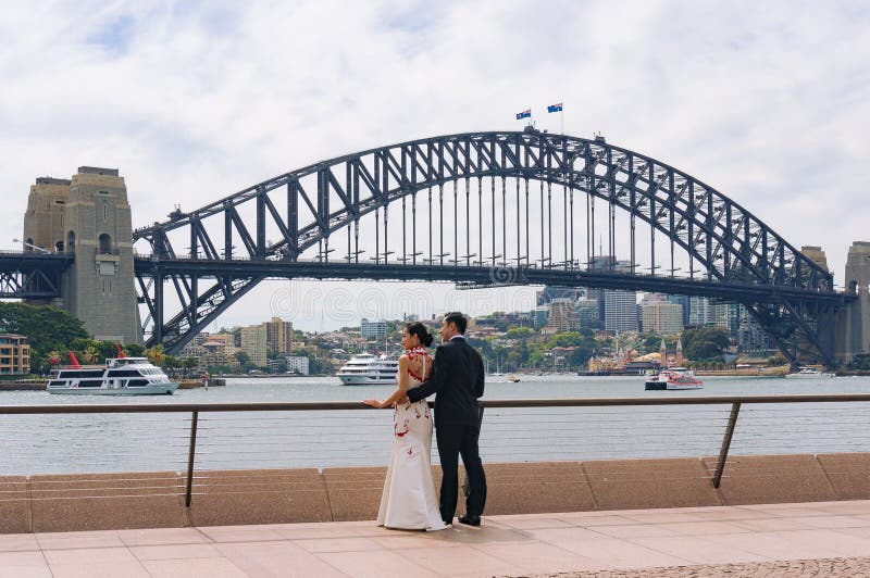 Young Asian couple posing against Sydney Harbour Bridge on background stock photo Young Asian couple posing against Sydney Harbour Bridge on background stock photo