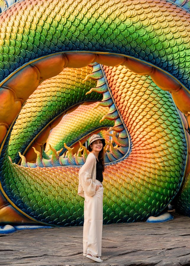 Young asian female tourist standing and posing for a photo with the body of colorful serpent sculpture in buddhism temple stock photography