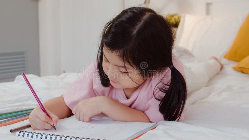 Young Asian girl drawing at home. Asia japanese woman child kid relax rest fun happy draw cartoon in sketchbook before sleep lying on bed, feel comfort and calm in bedroom at night concept. Young Asian girl drawing at home. Asia japanese woman child kid relax rest fun happy draw cartoon in sketchbook before sleep lying on bed, feel comfort and calm in bedroom at night concept