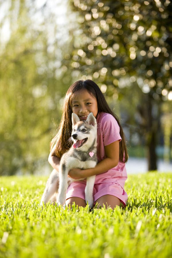 Young Asian girl hugging puppy sitting on grass