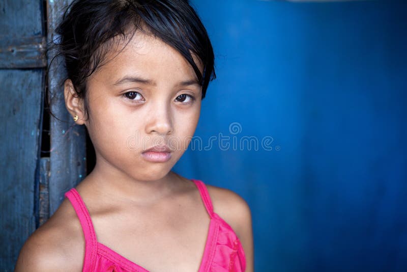 Young Filipina girl with sad and somber expression over blue, poverty in the Philippines. Young Filipina girl with sad and somber expression over blue, poverty in the Philippines.