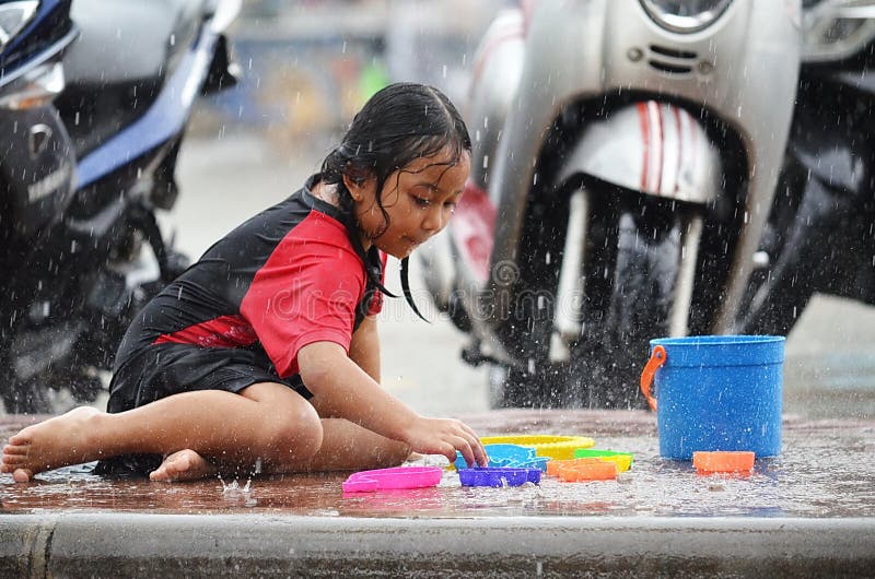 Young Asian girl selects a toy as she plays in the rain during monsoon season in Thailand. stock images Young Asian girl selects a toy as she plays in the rain during monsoon season in Thailand. stock images