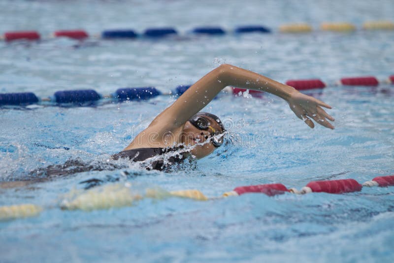 Young 10 year old asian girl swims freestyle with goggles and cap in a swimming pool. Young 10 year old asian girl swims freestyle with goggles and cap in a swimming pool