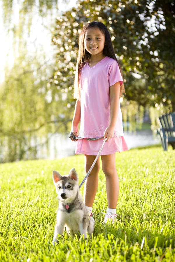 Young Asian girl walking puppy on leash on grass