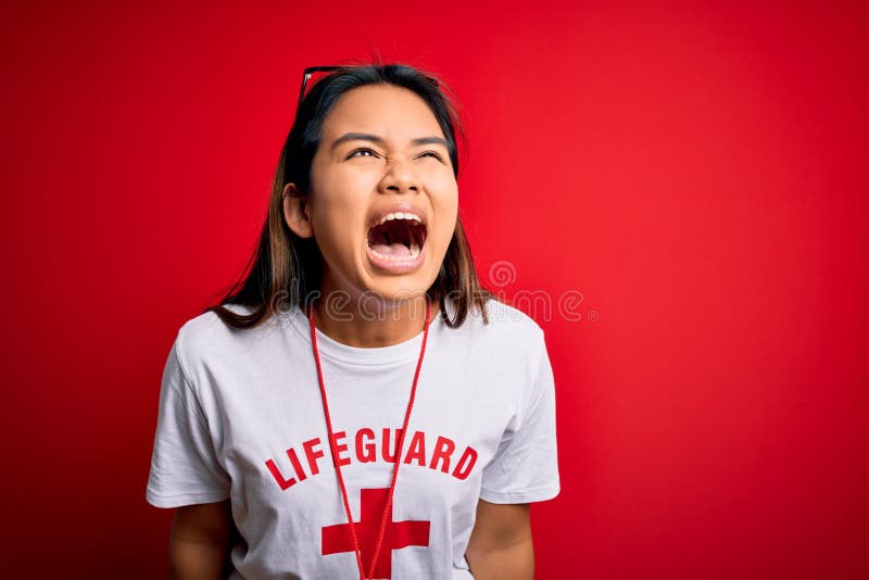 Young asian lifeguard girl wearing t-shirt with red cross using whistle over isolated background angry and mad screaming royalty free stock photo