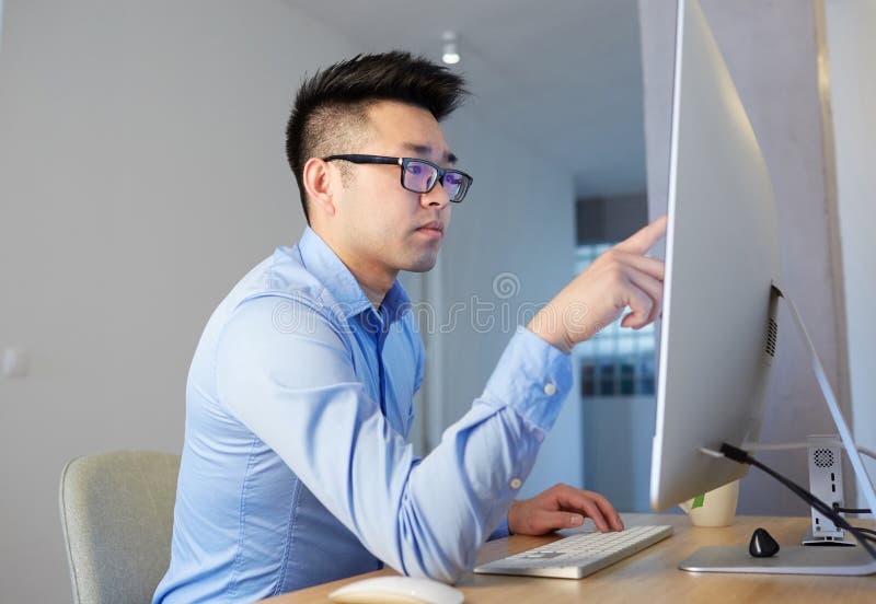 Young asian male programmer wearing shirt and glasses working while sitting in front of desktop computer at coworking stock photos Young asian male programmer wearing shirt and glasses working while sitting in front of desktop computer at coworking stock photos