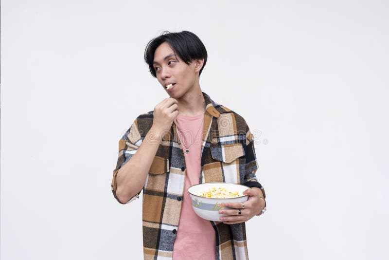 A young asian man eating popcorn in a relaxed casual way while watching a movie. Isolated on a white background stock images