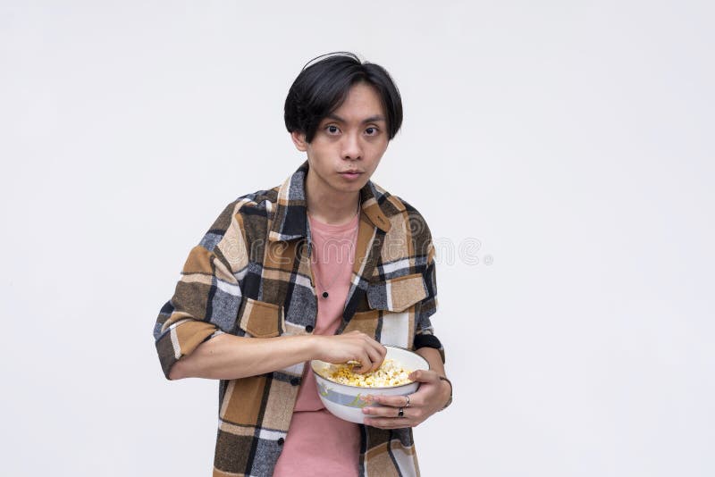 A young asian man looking spooked while holding a bowl of popcorn. Isolated on a white background royalty free stock photo