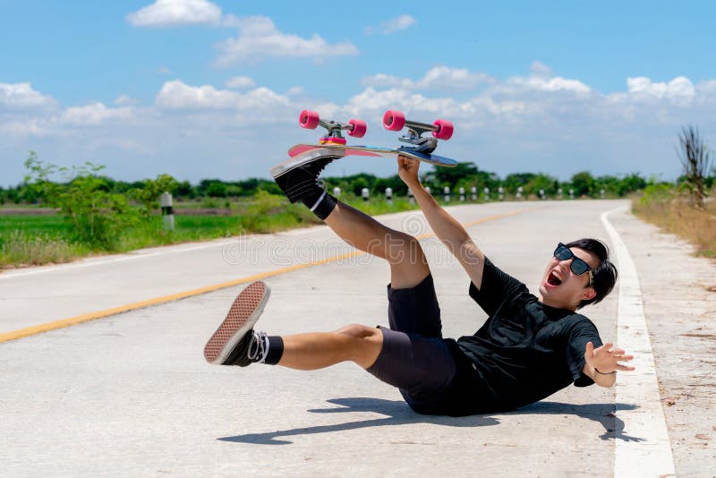 A young Asian man is wearing a black shirt and pants. play skateboard show an accident On a country road on a sunny day with sky.