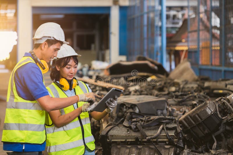 Young Asian man and woman staff worker working in dirty engine block scrap yard. engineer team using tablet computer together royalty free stock image