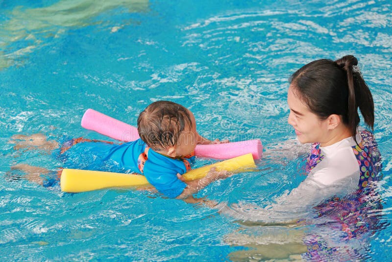 Young Asian mom teaching baby boy in swimming pool with noodle foam