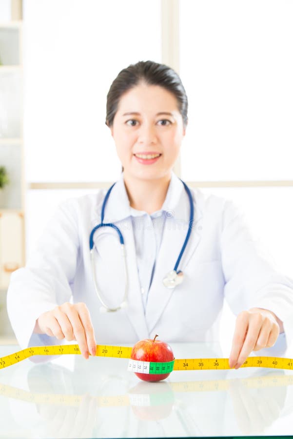 Young Asian Nutritionist Doctor Measuring an Apple Stock Photo Image