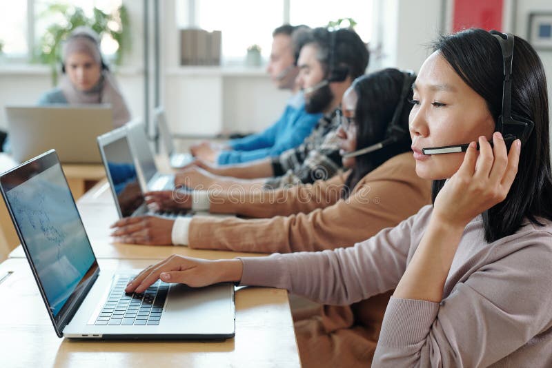Young Asian operator consulting clients online against her co-workers stock photos