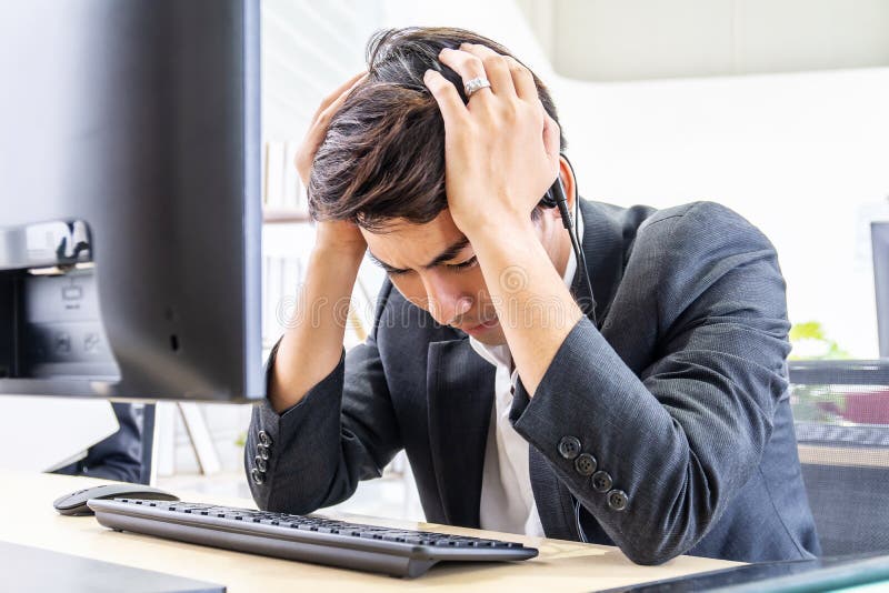 Young asian operator man wearing call center headset Feeling stress and headache from work in the office stock photo