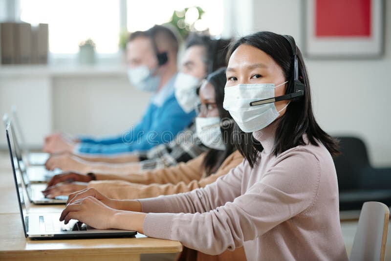 Young Asian operator in protective mask looking at camera stock images