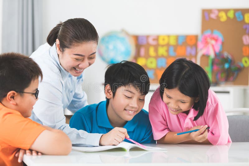 Young asian teacher helps young school kids in class. royalty free stock images Young asian teacher helps young school kids in class. royalty free stock images