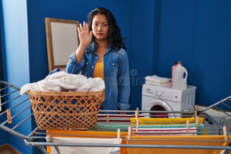 Young asian woman hanging clothes at clothesline doing stop sing with palm of the hand stock photos