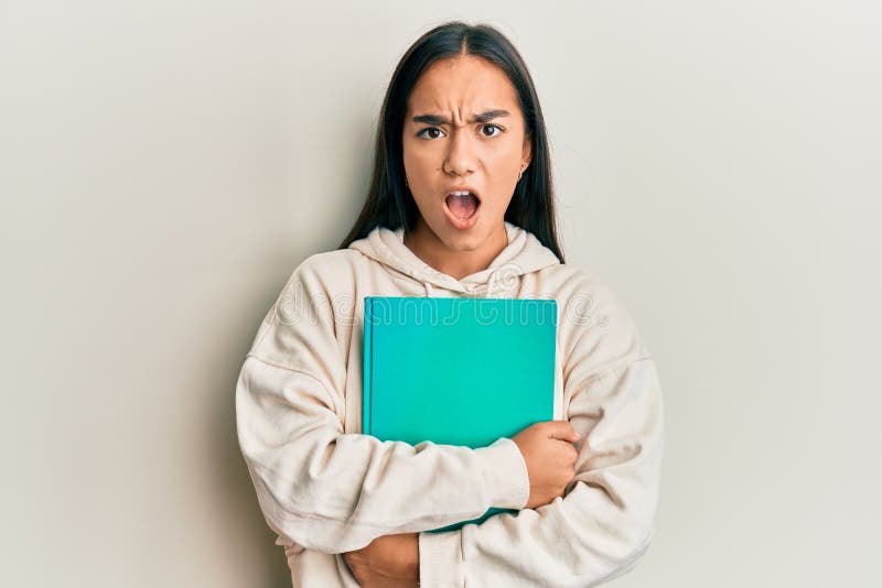 Young asian woman holding book in shock face, looking skeptical and sarcastic, surprised with open mouth stock photos