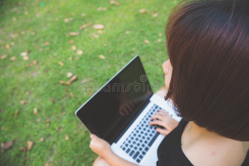Young asian woman legs on the green grass with open laptop. Girl hands on keyboard. Distance learning concept. Happy hipster young asian woman working on stock photography Young asian woman legs on the green grass with open laptop. Girl hands on keyboard. Distance learning concept. Happy hipster young asian woman working on stock photography