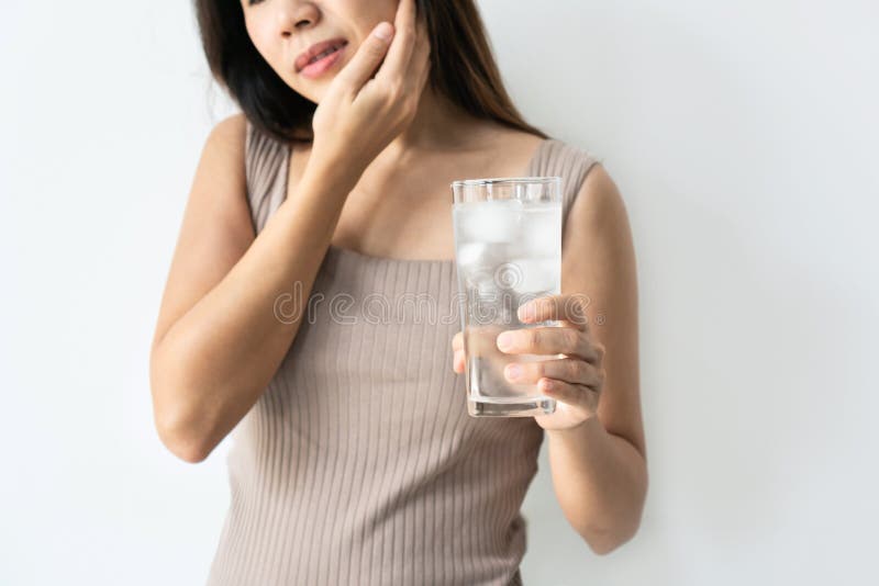Young Asian woman with sensitive teeth and hand holding glass of cold water with ice. Girl drinking cold drink, glass full of ice