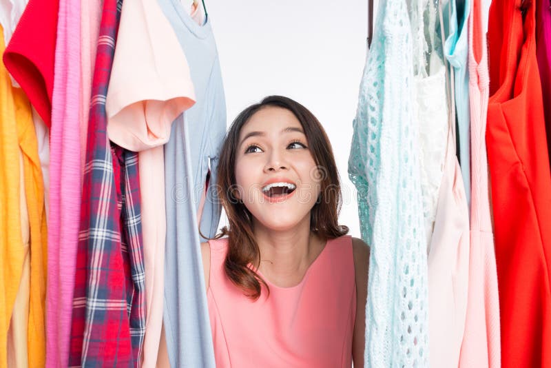 Young asian woman surprised in shop, peeking out through clothing in clothes rack stock photos Young asian woman surprised in shop, peeking out through clothing in clothes rack stock photos