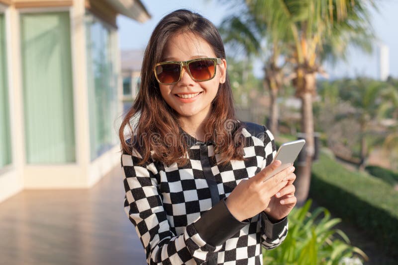 Young asian woman wearing sun glasses and smart phone in hand toothy smiling face