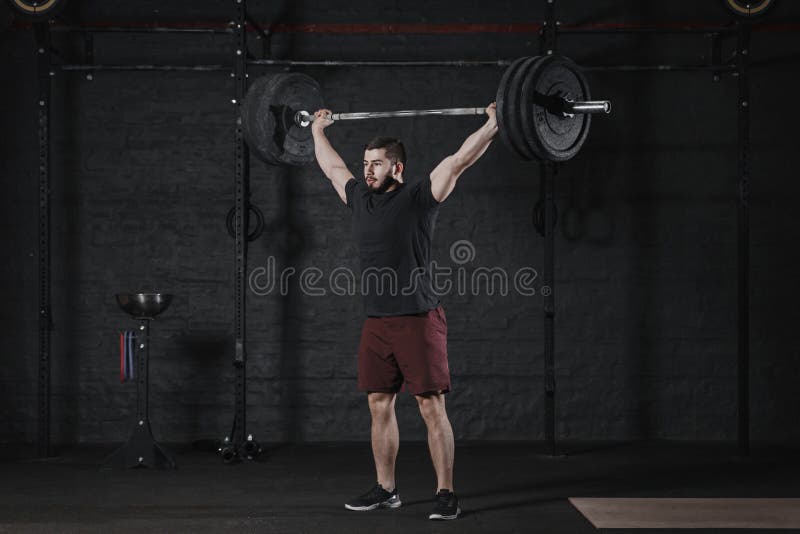 Young athlete lifting barbell overhead at the crossfit gym. Handsome man doing functional training. Practicing powerlifting. Workout exercises