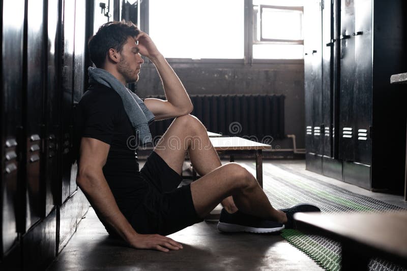 Young athletic Caucasian man sitting alone in dark gym locker room resting after workout. royalty free stock photography Young athletic Caucasian man sitting alone in dark gym locker room resting after workout. royalty free stock photography