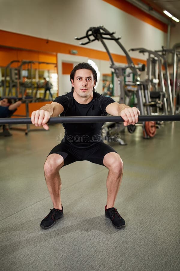 Young athletic man in black sportwear with bar of barbell flexing muscles in gym. royalty free stock photo Young athletic man in black sportwear with bar of barbell flexing muscles in gym. royalty free stock photo