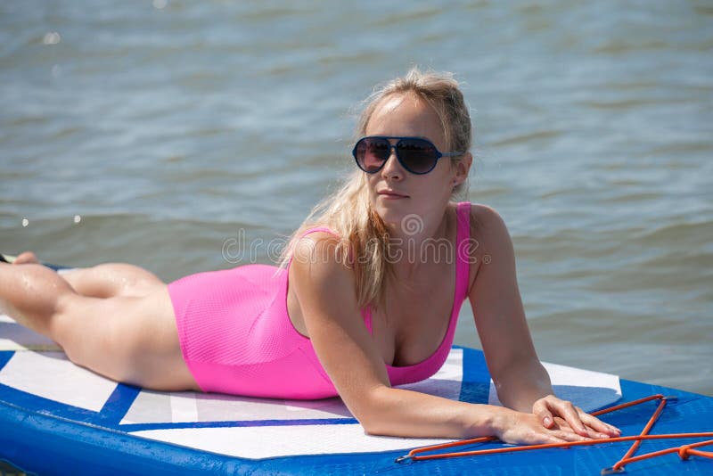 Young athletic woman in bright pink swimsuit doing fitness on a sup board with an oar on sea. Tropical travel and water activity stock photo Young athletic woman in bright pink swimsuit doing fitness on a sup board with an oar on sea. Tropical travel and water activity stock photo