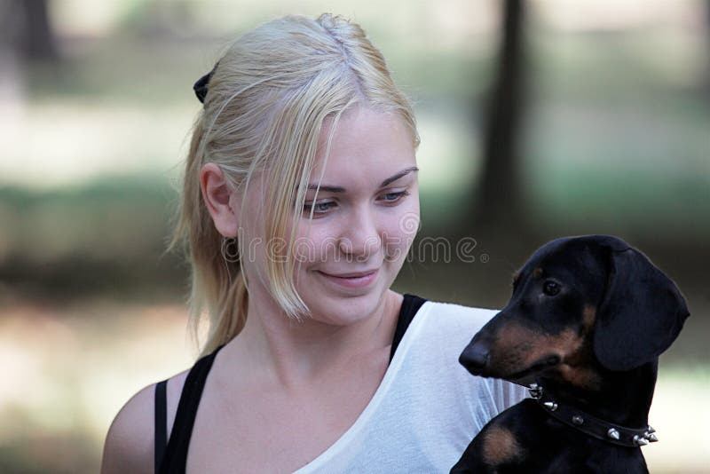 Young attractive blond smiling woman with a dachshund on her hand. She looks to the dog.