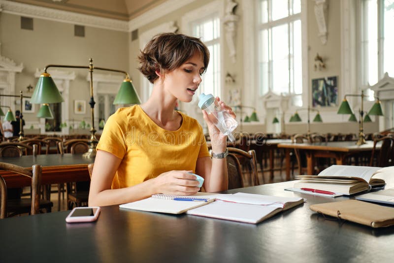 Young Attractive Casual Female Student Drinking Water while Study in