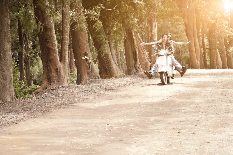 Young attractive couple traveling on scooter along dirt road