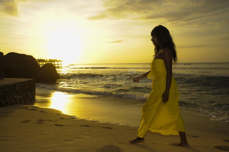 Glamorous African American black woman in chic and elegant summer dress posing relaxed walking on summer sunset beach