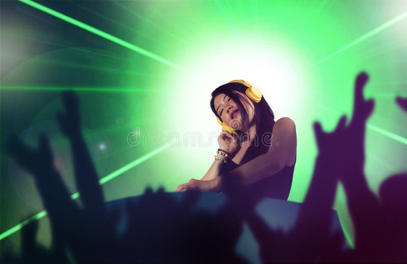 Young attractive and happy Asian Japanese DJ woman remixing using deejay gear and headphones at night club with lights background stock photo Young attractive and happy Asian Japanese DJ woman remixing using deejay gear and headphones at night club with lights background stock photo
