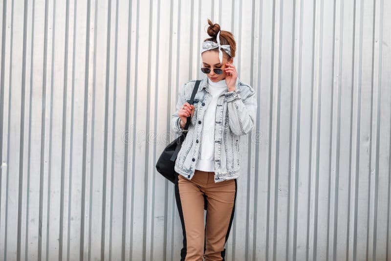 Young attractive hipster woman in knitted vintage white sweater in beige pants in a denim jacket in a bandana with royalty free stock image Young attractive hipster woman in knitted vintage white sweater in beige pants in a denim jacket in a bandana with royalty free stock image