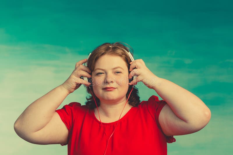 Young attractive plump woman with red hair with a displeased face takes off his headphones on a blue background royalty free stock image Young attractive plump woman with red hair with a displeased face takes off his headphones on a blue background royalty free stock image