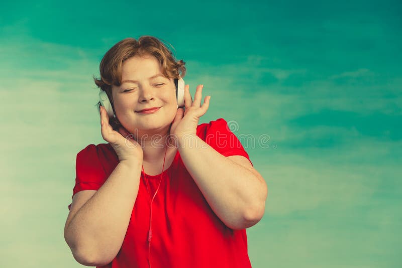 Young attractive plump woman with red hair listening to music with pleasure headphones with eyes closed on a green background stock photography Young attractive plump woman with red hair listening to music with pleasure headphones with eyes closed on a green background stock photography