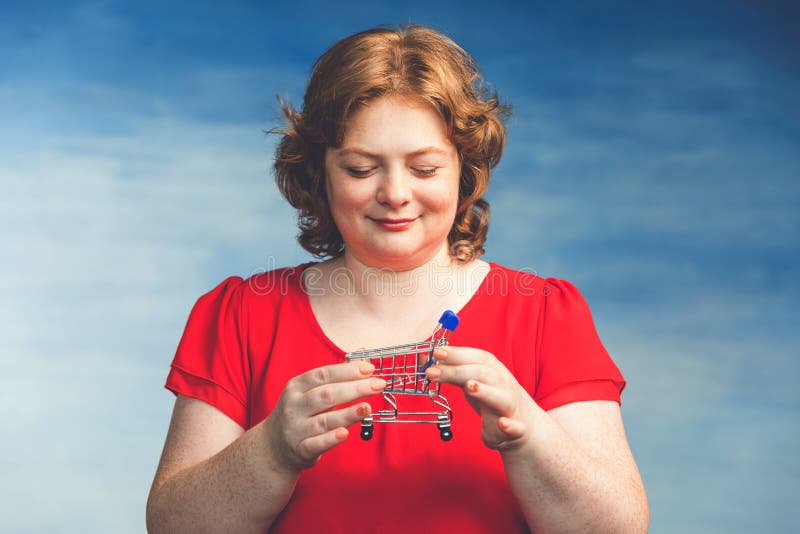Young attractive plump woman with red hair looks at the little cart from the store in her hands royalty free stock photos Young attractive plump woman with red hair looks at the little cart from the store in her hands royalty free stock photos