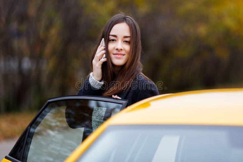 Young attractive smiling woman speaking on mobile phone near taxi