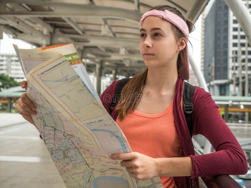 Young Attractive traveler woman holding location map in her hands while looking for some direction on street, travel or exploring royalty free stock photography Young Attractive traveler woman holding location map in her hands while looking for some direction on street, travel or exploring royalty free stock photography
