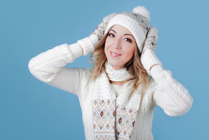 Young and attractive woman in a knitted sweater. Pulls cap, blue background