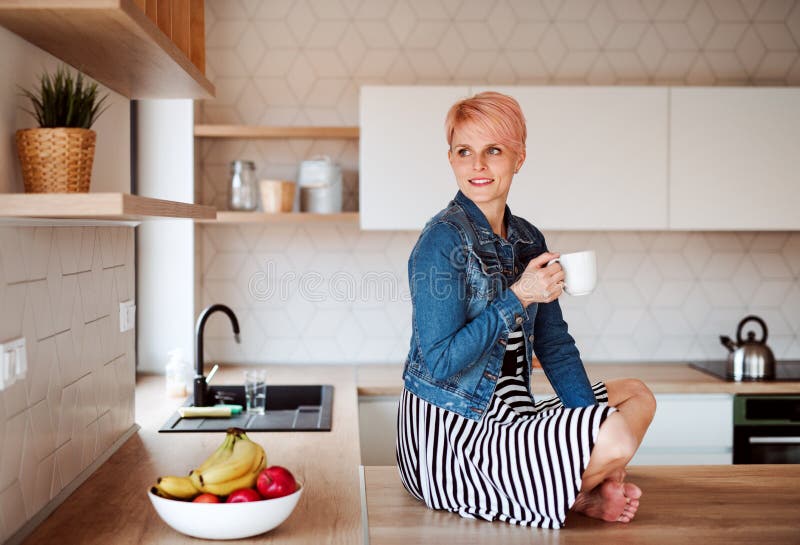 A Young Attractive Woman Sitting On A Counter In A Kitchen At Home