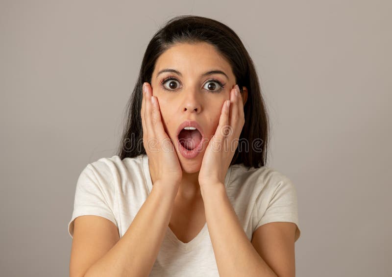 Close up portrait of a beautiful young latin hispanic woman with a surprised and shocked face looking amazed with wide eyes and mouth open.Human facial expressions and emotions. Gray background. Close up portrait of a beautiful young latin hispanic woman with a surprised and shocked face looking amazed with wide eyes and mouth open.Human facial expressions and emotions. Gray background