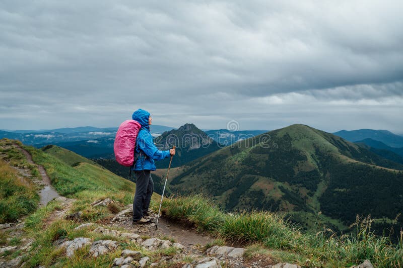 Mladá batôžkárka oblečená v modrom obleku do dažďa so sledovacími palicami s ruksakom si užíva slovenskú Malú Fatru.