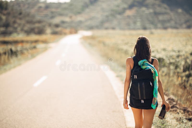 Young backpacking adventurous woman hitchhiking on the road.Traveling backpacks volume,packing essentials.Travel lifestyle