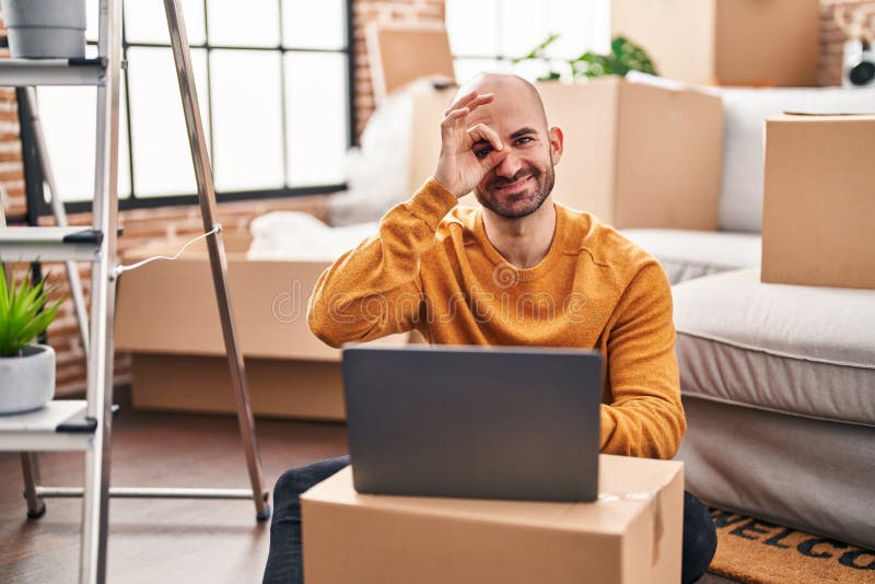 young-bald-man-with-beard-moving-to-a-new-house-using-laptop-smiling-happy-doing-ok-sign-with