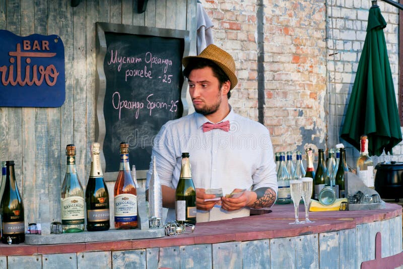 Smiling male bartender wiping a glass and looking away. Barista in