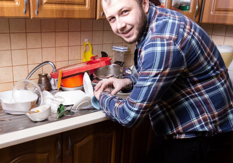 A young bearded guy looks at his watch and is happy by the amount of dirty dishes lying in the kitchen sink. He have time to wash royalty free stock photos A young bearded guy looks at his watch and is happy by the amount of dirty dishes lying in the kitchen sink. He have time to wash royalty free stock photos