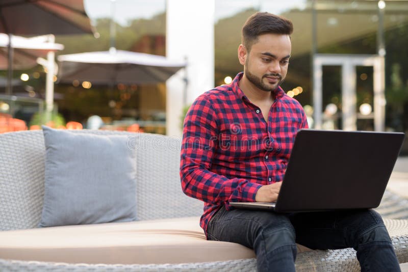 Young bearded Indian businessman relaxing at the mall in Bangkok stock photo Young bearded Indian businessman relaxing at the mall in Bangkok stock photo
